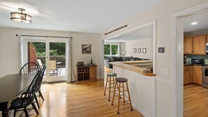 A modern kitchen with wooden cabinets, a central island with stools, and a dining area with a table and chairs. - Timber Creek Retreat w/ Free Shuttle & Fireplace! (Dover)