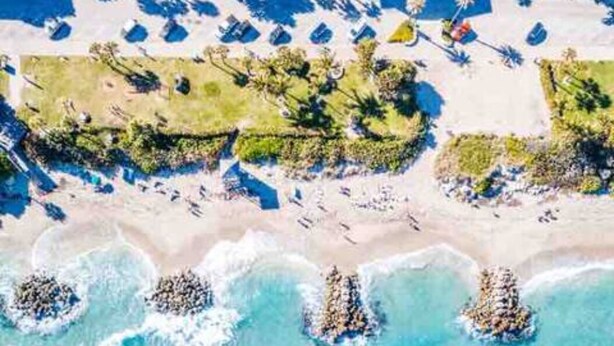 An aerial view of a beach with clear blue waters, a sandy shore, and several palm trees. - 4BR/3BA Mini-Resort Near Beach heated Pool & Spa (Pompano Beach)