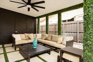 Une terrasse extérieure avec un ventilateur de plafond noir, un canapé beige et une table basse en bois.