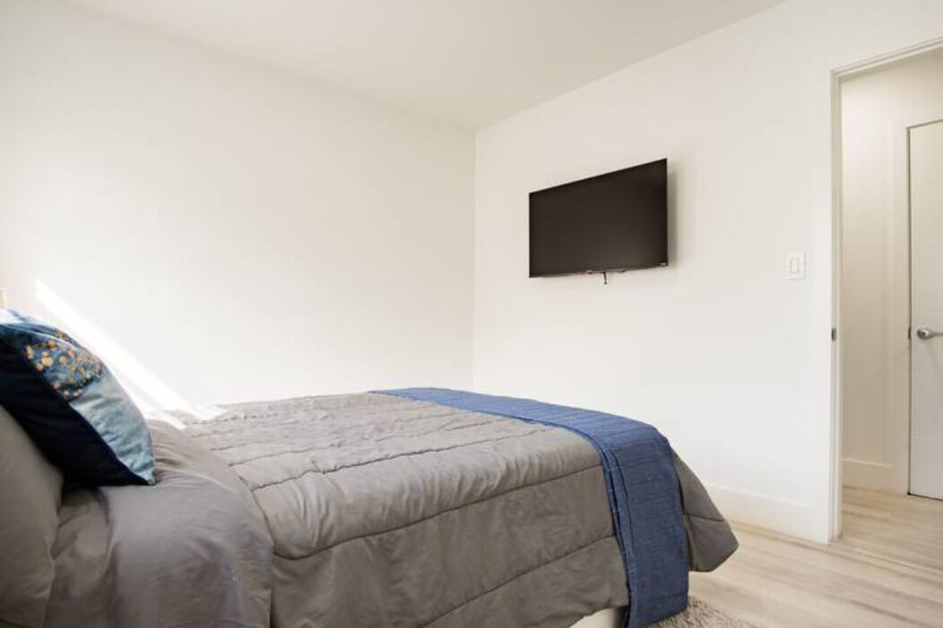 A bedroom with a bed, a flat-screen TV mounted on the wall, and a door.