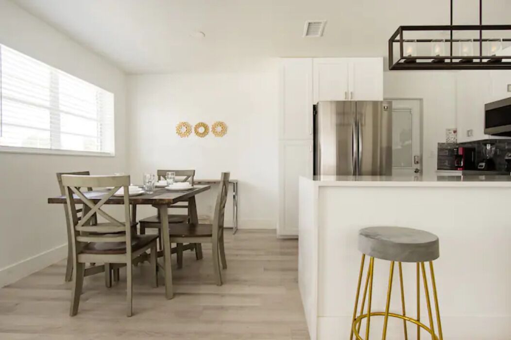 A modern kitchen with white cabinetry, a stainless steel refrigerator, and a bar area with a stool.