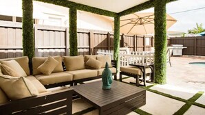 An outdoor patio with a beige sofa, a wooden coffee table, and a white fence. - 4BR/3BA Mini-Resort Near Beach heated Pool & Spa (Pompano Beach)