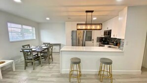 A modern kitchen with a white countertop, stainless steel appliances, and a bar area with stools. - 4BR/3BA Mini-Resort Near Beach heated Pool & Spa (Pompano Beach)