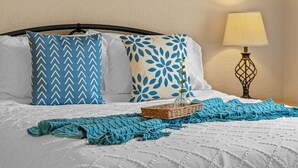 Een net opgemaakt bed met een kussen met dessin, een blauwe gebreide deken en een bedlampje.