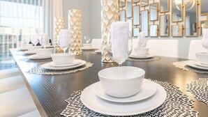 Un coin repas avec une longue table dressée pour le repas, comprenant des assiettes et des bols blancs, ainsi qu’un verre à vin et une serviette.