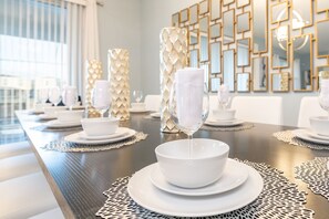 Enjoy a sophisticated dining experience in this elegantly set room, featuring a long table with fine china and a stylish geometric wall paneling.