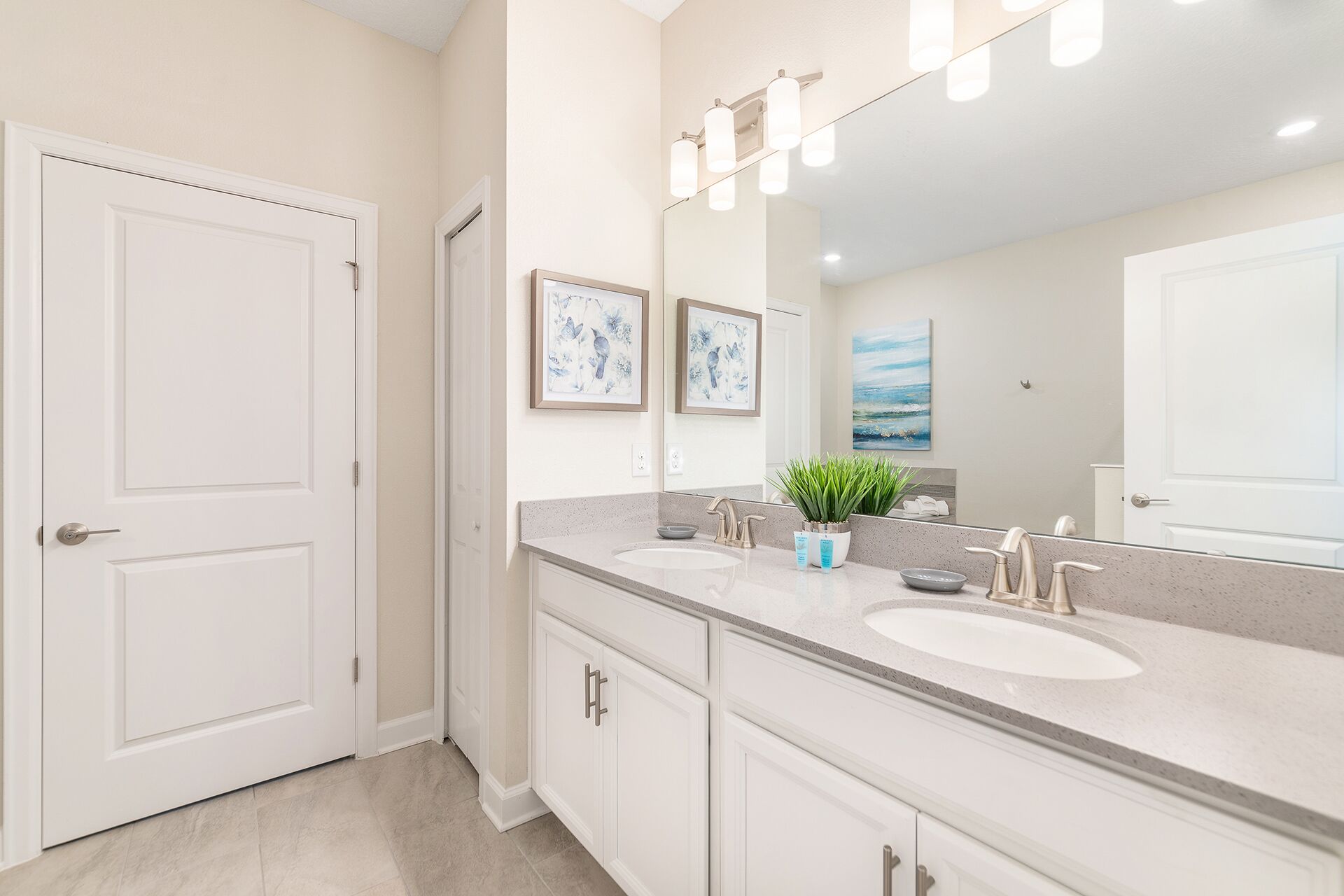 A modern bathroom with two sinks, a large mirror, and framed artwork on the wall.