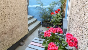 Un étroit couloir extérieur avec un mur bleu, un escalier en béton et un banc en bois.
