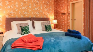 Une chambre d’hôtel avec un lit, des oreillers, une table de chevet, une lampe et une porte.