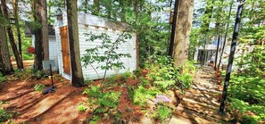 A wooden cabin surrounded by trees, with a dirt path leading to it. - Stabbin Cabin #2 on Grant Island-HotTub,Boat,Pets (BRANTINGHAM)