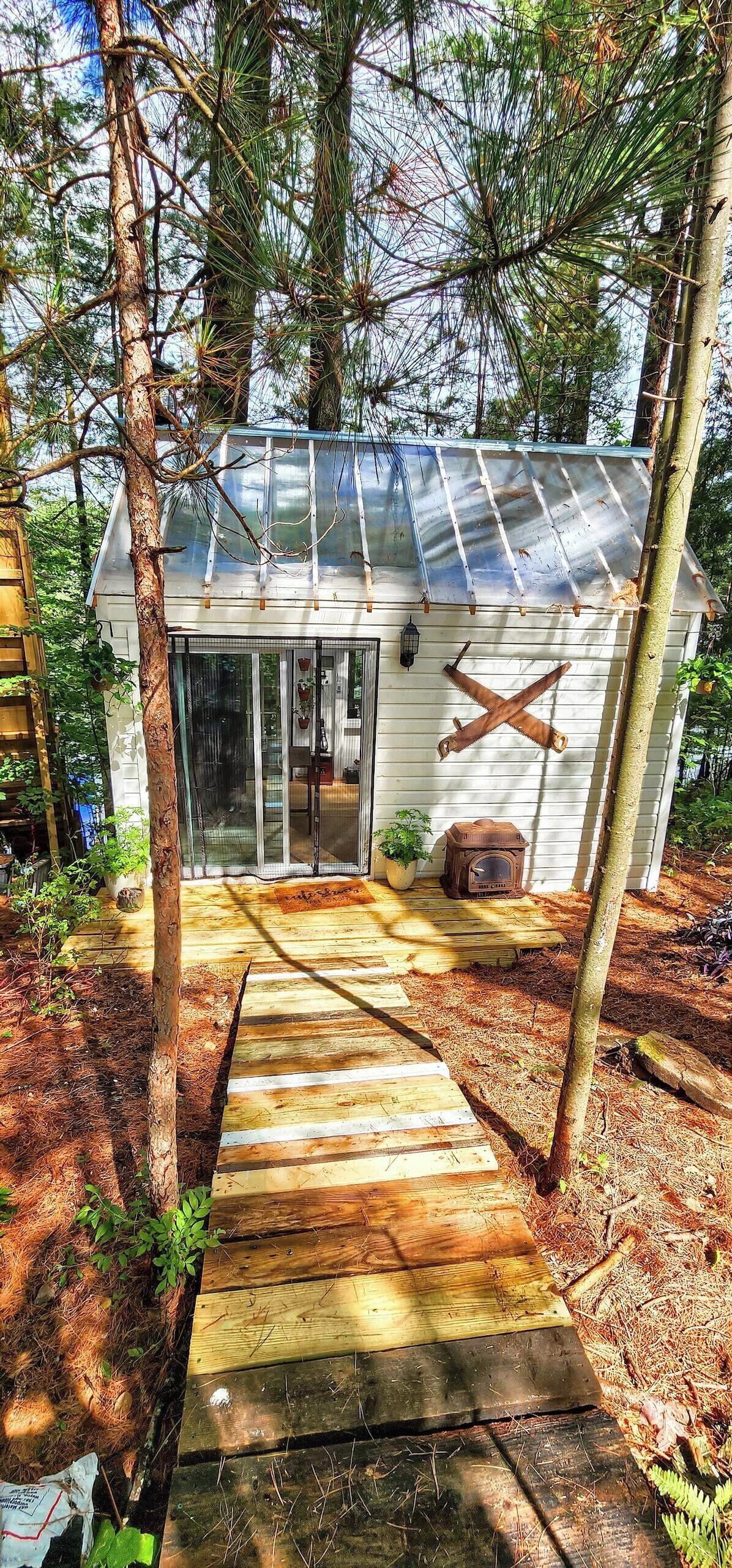 A wooden deck leading to a house with a metal roof, surrounded by trees.