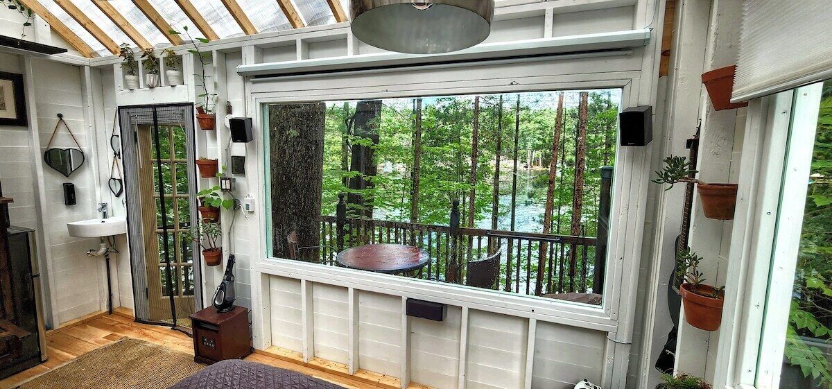 Ein Zimmer mit großem Fenster und Blick auf eine bewaldete Landschaft, einem kleinen Tisch und einer eingebauten Bank.