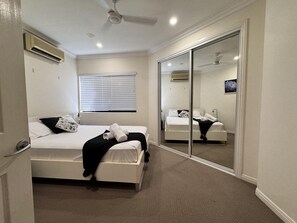 Un dormitorio con una cama, una ventana con persianas, un ventilador de techo y una puerta corrediza con espejo.