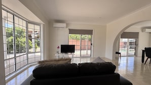 A spacious living room with a large window, a flat-screen TV, a sofa, and a dining area. - Comfort, Convenience, and Space – Modern Family Living in Annandale - Comfort, Convenience, and Space – Family Living in Annandale (Annandale)