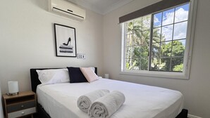 A neatly made bed with white linens and rolled towels, a bedside table with a lamp, and a window with a view of greenery. - Comfort, Convenience, and Space – Modern Family Living in Annandale - Comfort, Convenience, and Space – Family Living in Annandale (Annandale)