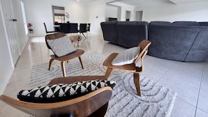 A spacious living room with a grey sectional sofa, two wooden chairs with patterned cushions, a dining table with chairs, and a dog. - Comfort, Convenience, and Space – Modern Family Living in Annandale - Comfort, Convenience, and Space   – Family Living in Annandale (Annandale)