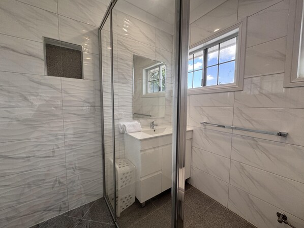 A modern bathroom with a glass shower enclosure, a sink, and a window.