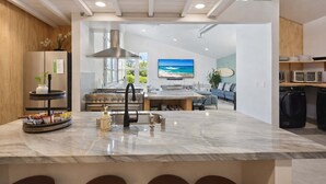 A modern kitchen with a central island, stainless steel appliances, and a large window overlooking a beach. - Resort Perks: 17-bed Surf lof.t private deck (San Diego)