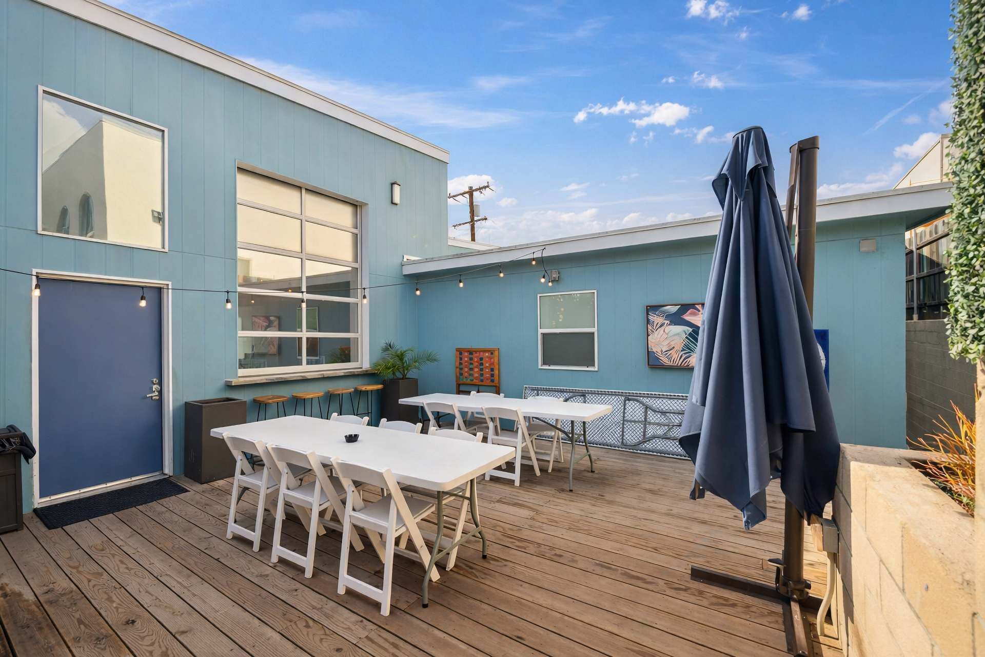 An outdoor patio with wooden flooring, white tables, and chairs. There are umbrellas and a large window on the building.