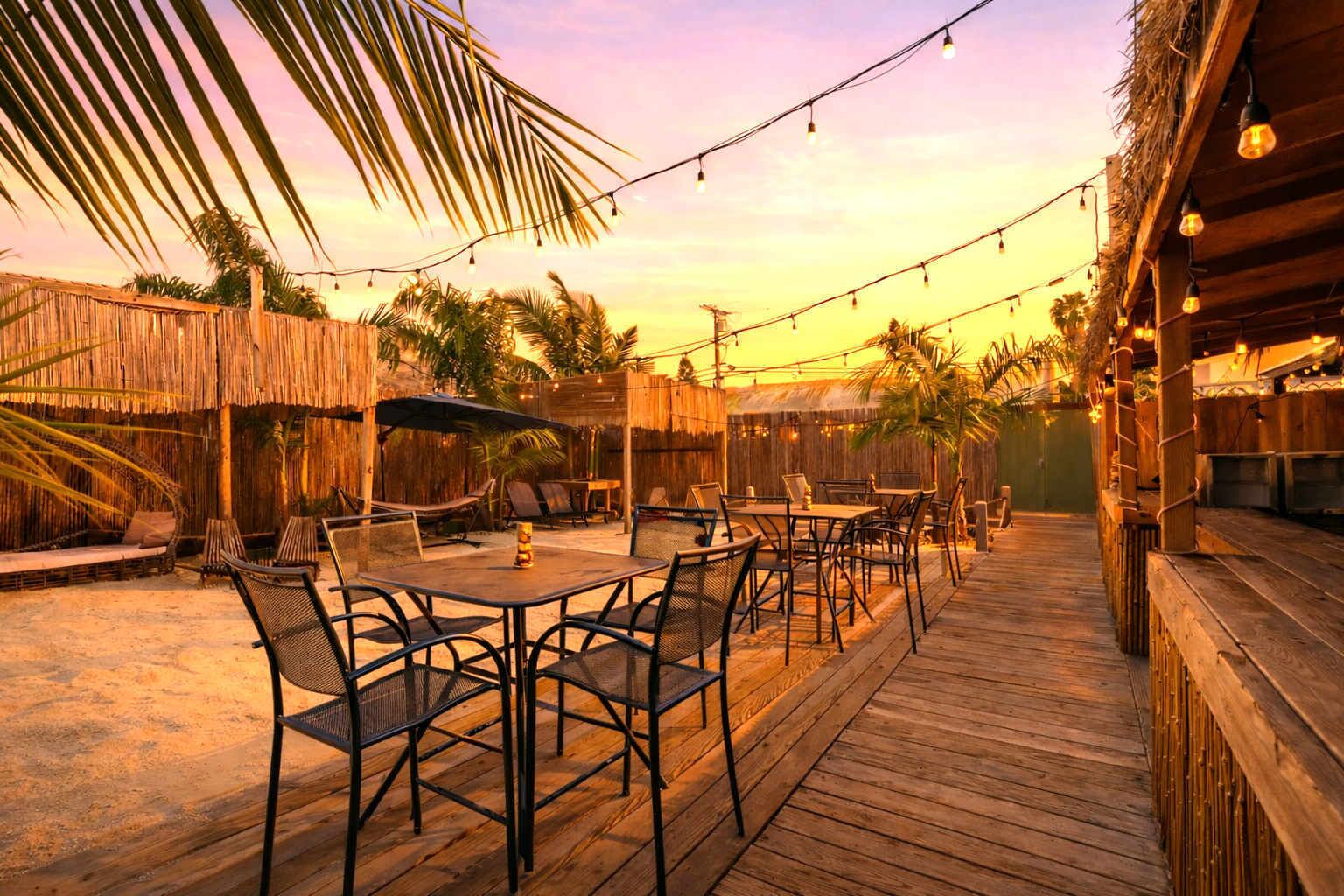 Een terras buiten met houten vloer, tafels, stoelen en lichtslingers.