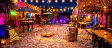 A beachside restaurant with outdoor seating, string lights, and a thatched-roof structure.