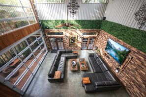 Un amplio patio interior con un sofá modular grande, un ventilador de techo y un televisor montado en la pared.