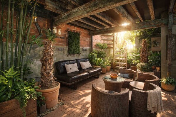 Un patio acogedor con un sofá de cuero, sillas de mimbre y plantas en macetas.