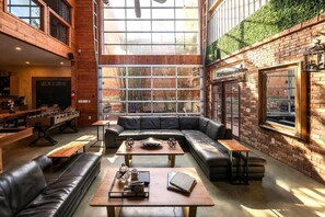 A spacious lounge area with a leather sofa, wooden tables, and a large window offering a view of the outdoors. - 9BR Bamboo Loft * Near Downtown 21 bed 26 capacity (San Diego)