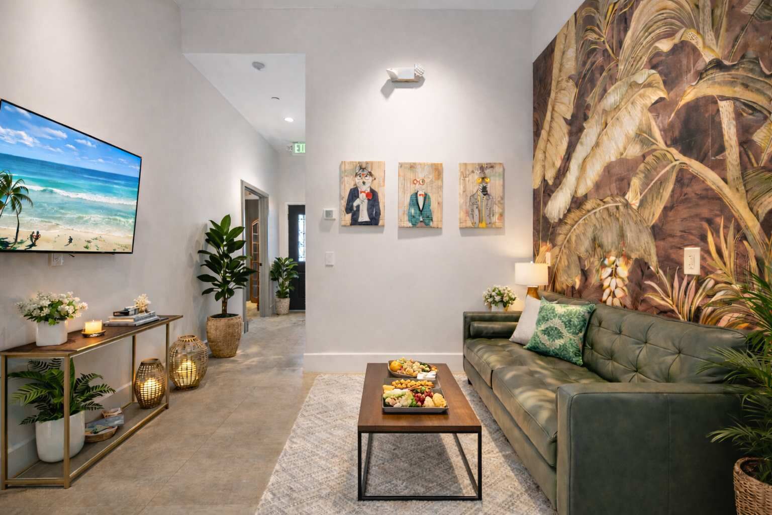 Un salon moderne avec une grande télévision, un canapé, une table basse sur laquelle on a disposé des fruits, et une fresque murale aux motifs tropicaux.