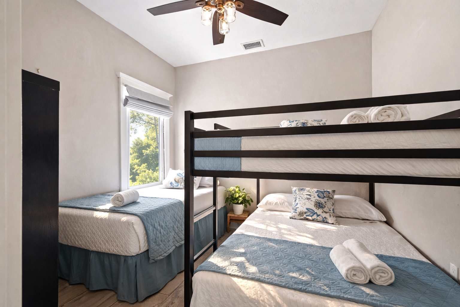 A room with bunk beds, a window with blinds, a ceiling fan, and a potted plant.