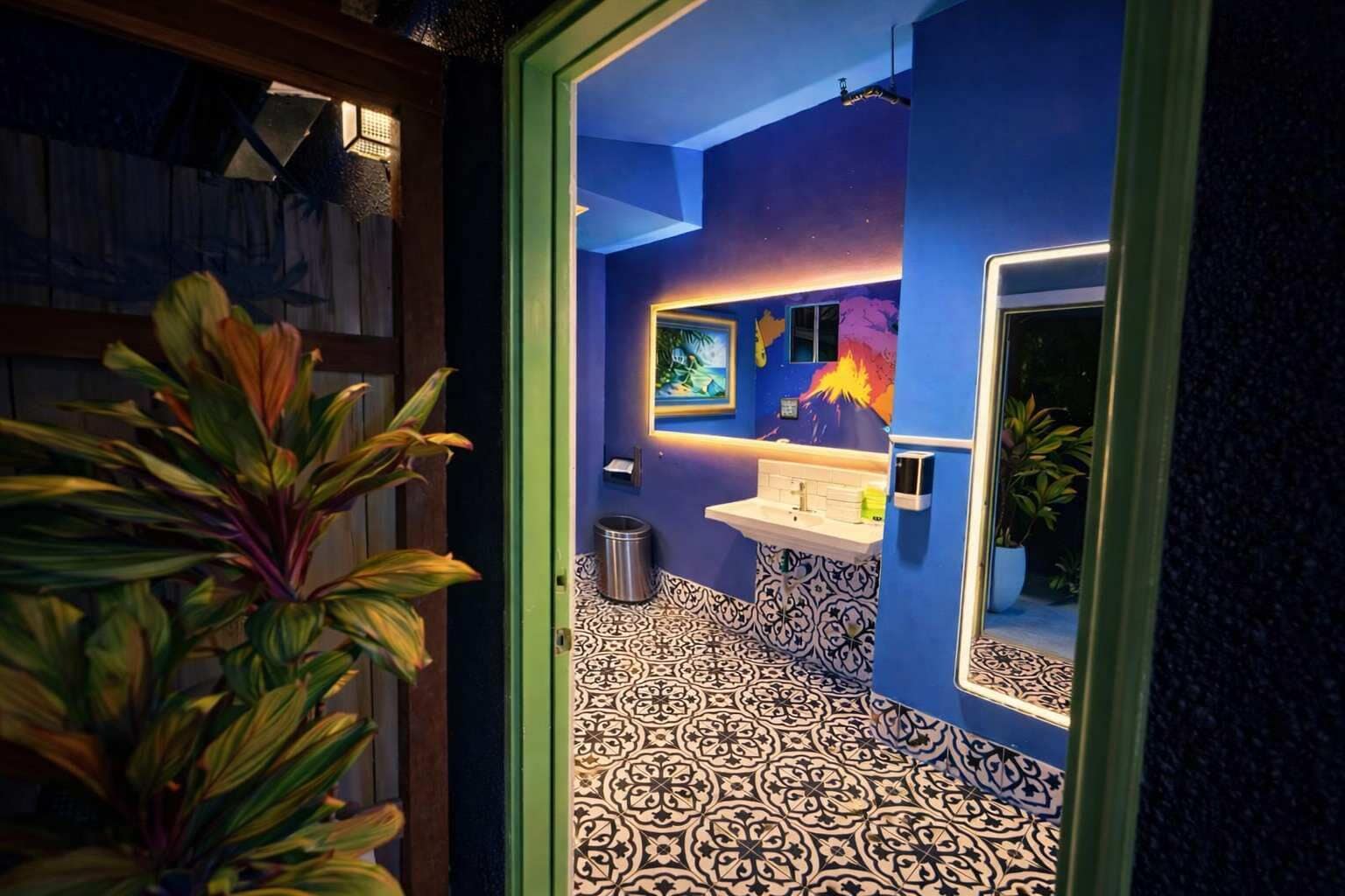 Un baño con pared azul, un lavabo, un espejo y baldosas de suelo estampadas.