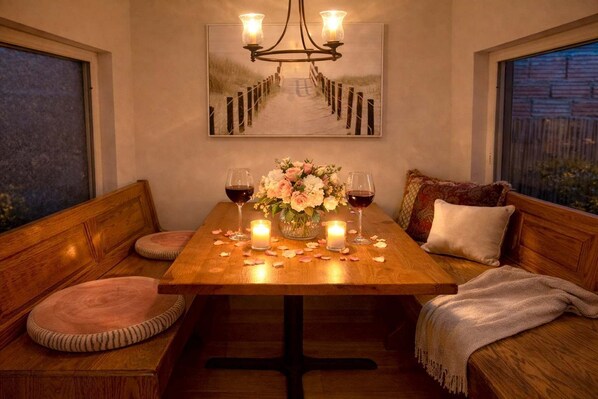 A cozy dining area with a wooden table, two candles, a vase of flowers, and wine glasses.