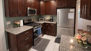 A kitchen with dark wood cabinets, stainless steel appliances, granite countertops, and a refrigerator with a note on it. - Bamboo House  (Downtown, Convention Center) 3BR (San Diego)
