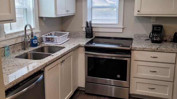 A modern kitchen with white cabinets, a stainless steel range, a dishwasher, and a coffee maker. - Cozy 3/2 cottage near Memorial Hospital. (Lake Charles)