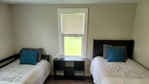 A bedroom with two single beds, a small table, and a window with blinds. - Cozy 3/2 cottage near Memorial Hospital. (Lake Charles)