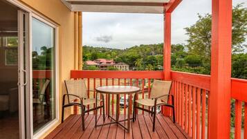 Una terraza de madera con un ventanal de vidrio que da a una habitación, una mesa redonda con sillas y una barandilla roja.