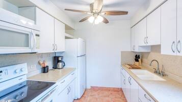 Cocina compacta con gabinetes blancos, microondas, estufa, cafetera y ventilador de techo.