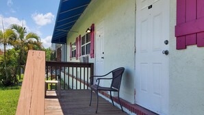 A wooden deck with a bench, a white door with a number, and a blue awning. - Quaint, Lakeside Budget Hotel Room (Everglades City)