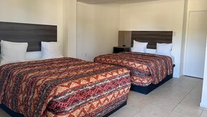 A hotel room with two beds, each with a patterned bedspread and white pillows. The room has a tiled floor and a plain white ceiling. - Quaint, Lakeside Budget Hotel Room (Everglades City)