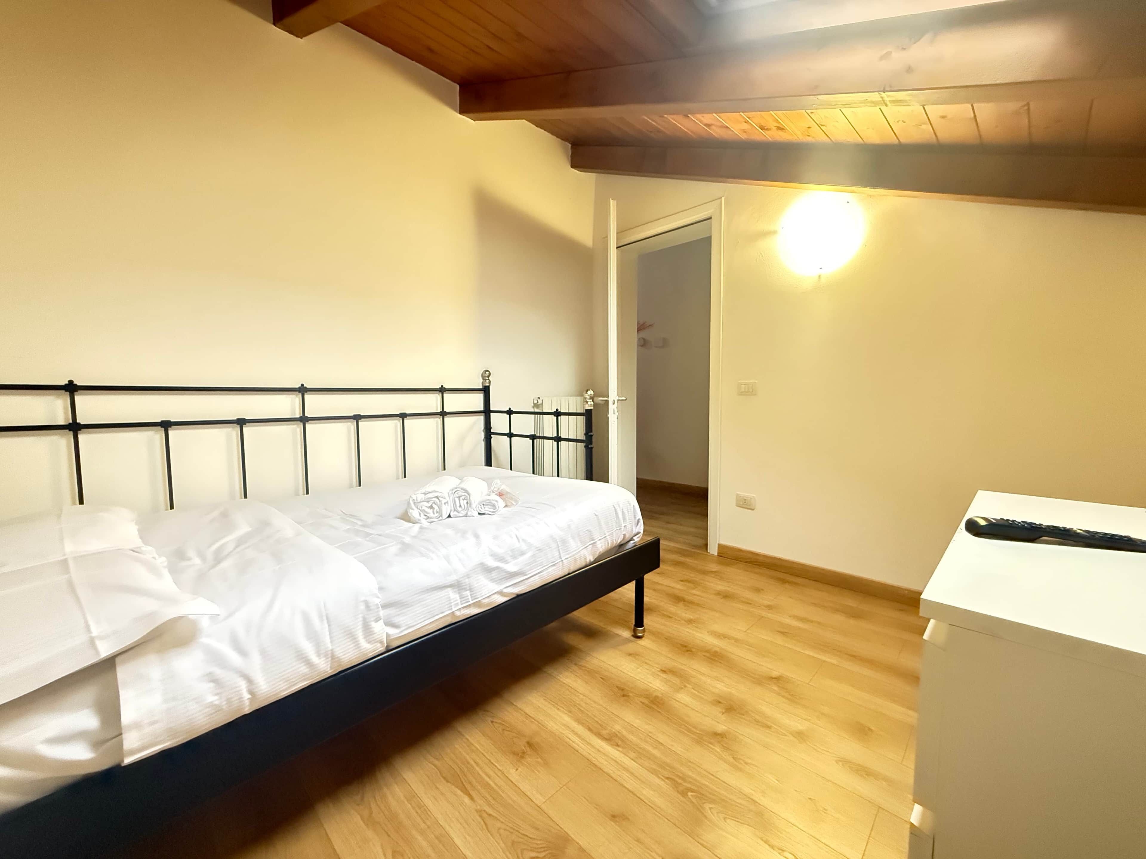 Une chambre à coucher avec un lit, un plancher en bois, une armoire blanche et une porte donnant sur une autre pièce.
