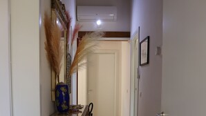 Um corredor com piso de madeira, um armário decorativo, um vaso com plantas secas e um extintor de incêndio.