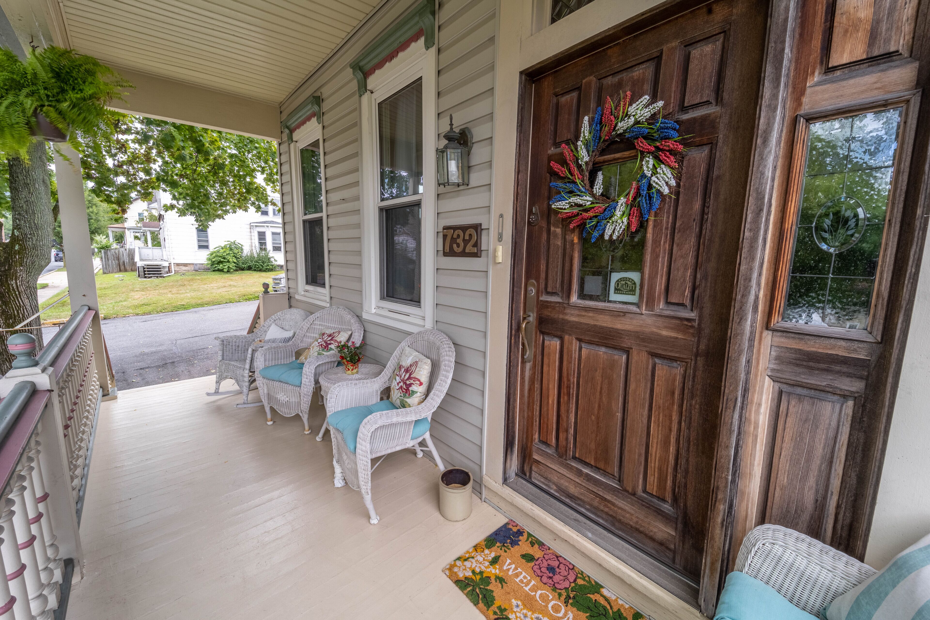 A porch with wicker chairs and a wooden door with a wreath.