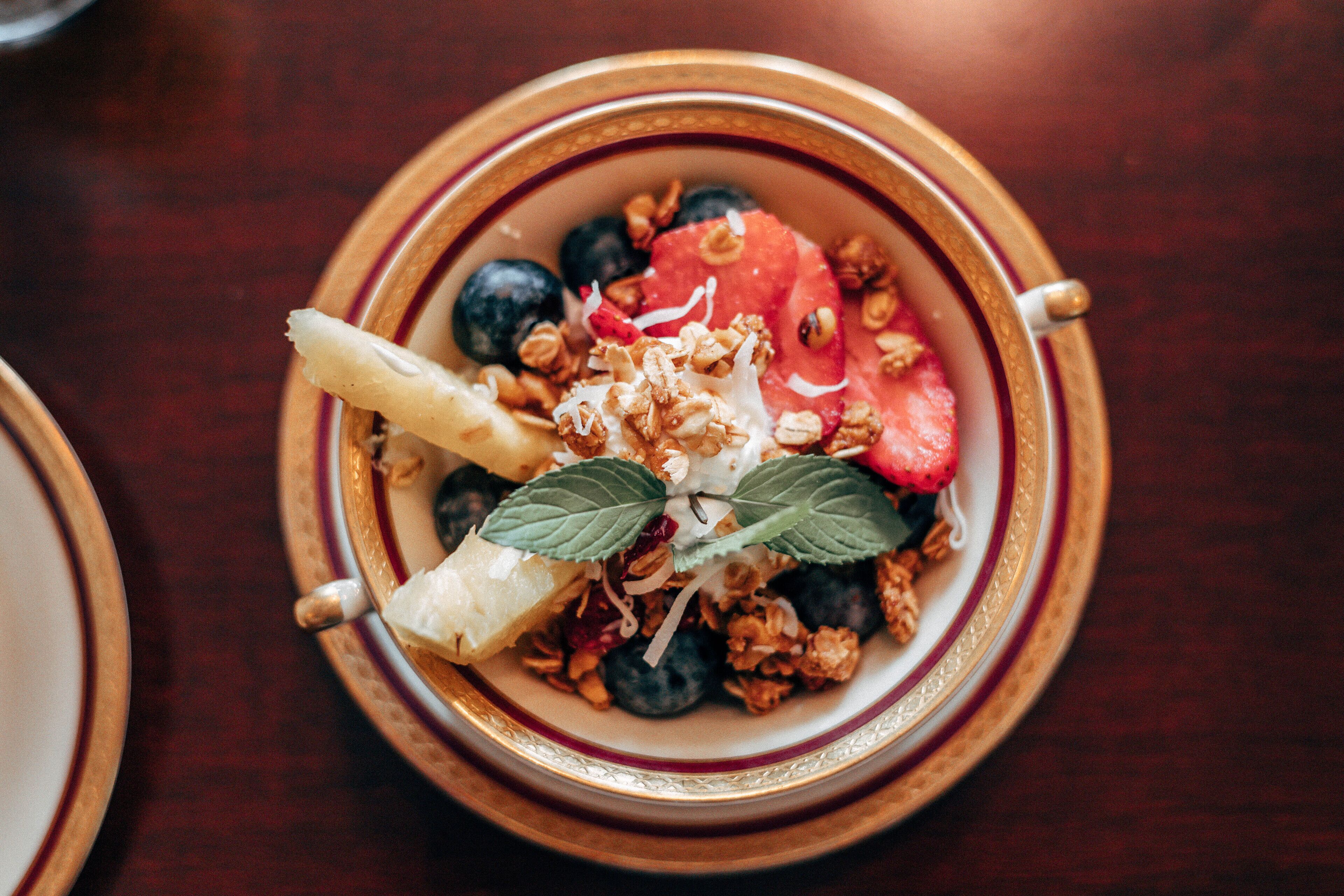 A bowl of yogurt with granola, blueberries, and a slice of watermelon on a wooden table.