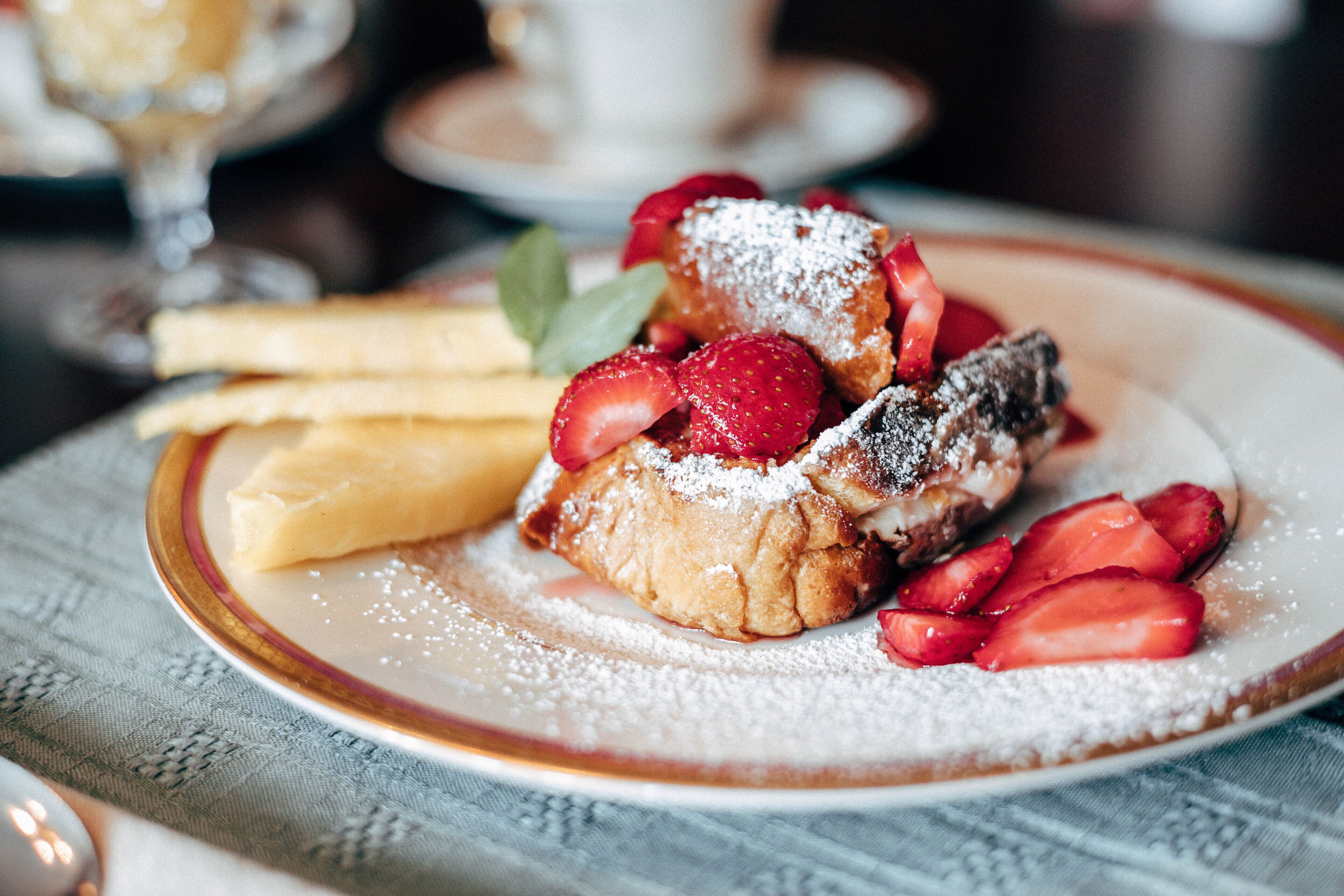 A plate with a dessert consisting of a pastry, strawberries, and powdered sugar.