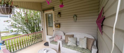 A porch with wicker furniture, a colorful rug, and hanging flowers.