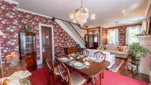 A dining area with a wooden table set for four, surrounded by chairs. A chandelier hangs from the ceiling, and a staircase is visible in the background leading to another room. - The Bella Victoria- Adult Only (Jim Thorpe)