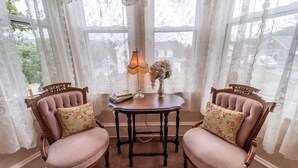 A room with two wooden chairs with floral cushions, a small table with a lamp, and lace curtains. - The Bella Victoria- Adult Only (Jim Thorpe)