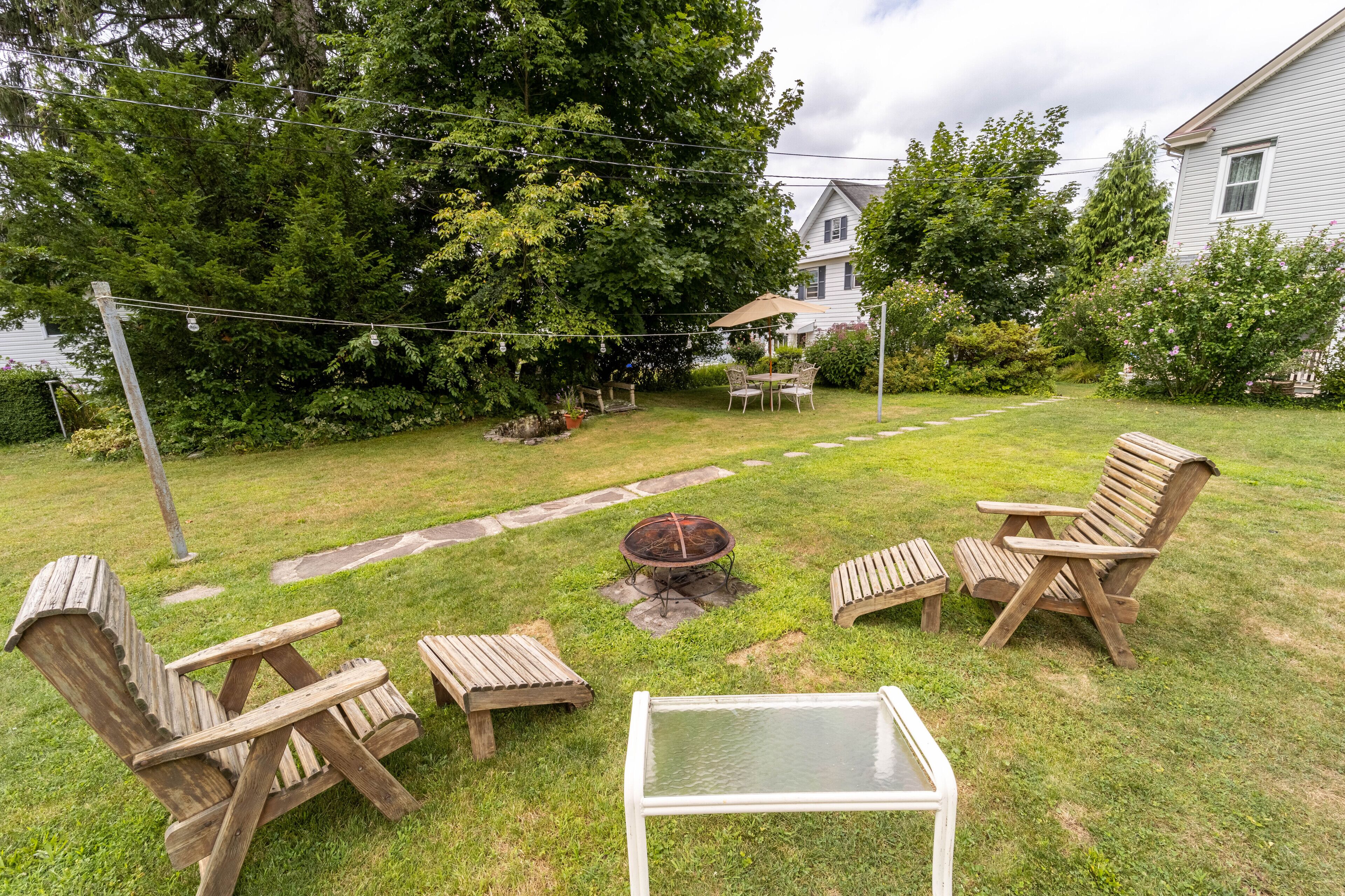 A backyard with a fire pit, wooden chairs, and a table.