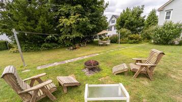 A backyard with a fire pit, wooden chairs, and a table.
