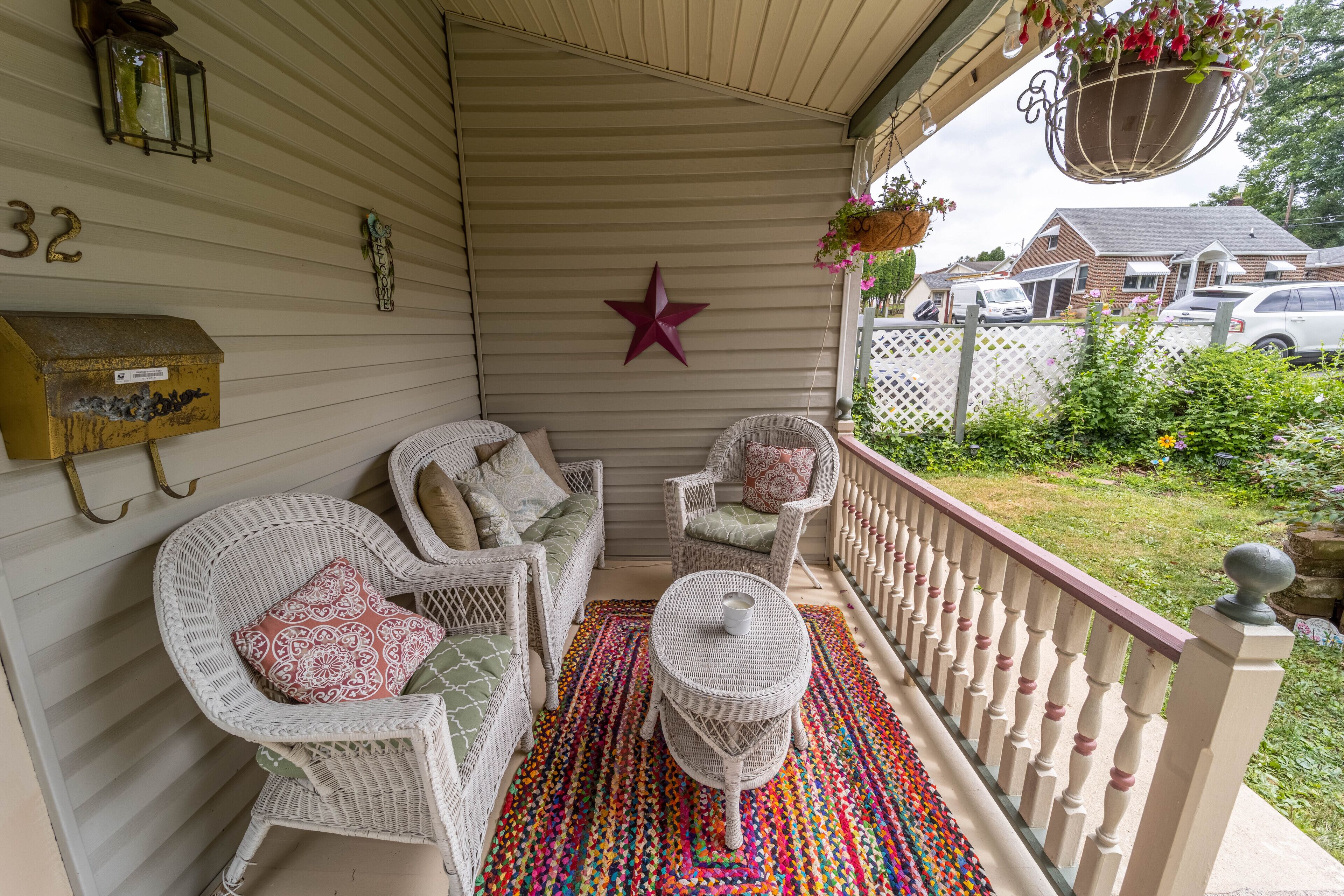 A covered porch with wicker furniture, a star decoration, and a colorful rug.